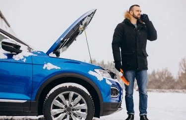 Чоловік біля розбитої машини на сніжному дорозі