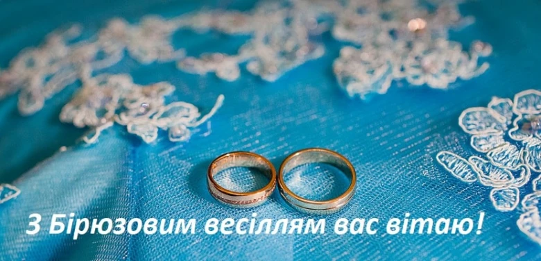 Золоті весільні кільця на блакитному фоні з вишивкою.