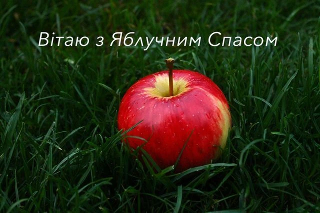 Червоне яблуко на траві з привітанням Яблучний Спас.